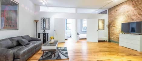 Een moderne woonkamer met een leren bank, een salontafel en een flatscreen televisie tegen een bakstenen muur.