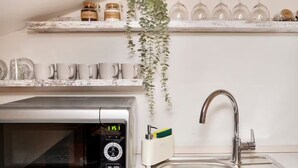 Une cuisine équipée d’un four à micro-ondes, d’un évier et d’étagères où sont rangés des bocaux et des tasses.