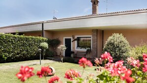 Un immeuble résidentiel doté d’un porche abrité, d’une cheminée et d’un jardin bien entretenu agrémenté de fleurs rouges.