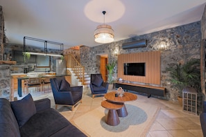 A modern living room with a stone wall, a TV mounted on the wall, a wooden coffee table, and a sofa.