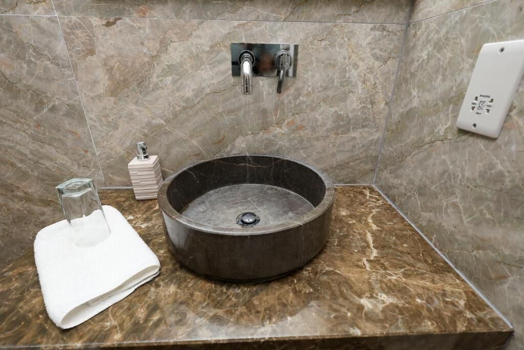 Un baño con un lavamanos redondo, un dispensador de toallas y un cabezal de ducha manual.