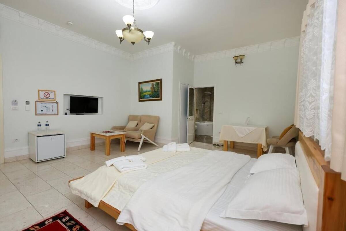 A bedroom with a bed, a chair, a small table, a TV, a desk, a wardrobe, and a bathroom door.