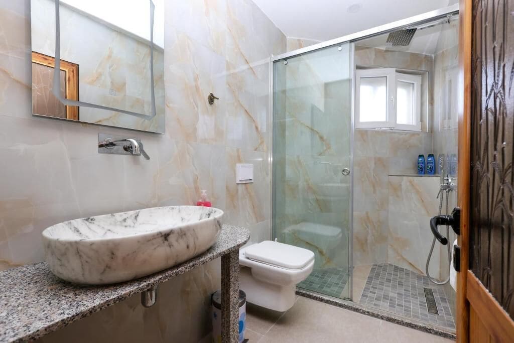 Un baño con lavamanos de mármol, inodoro y ducha con mampara de vidrio.