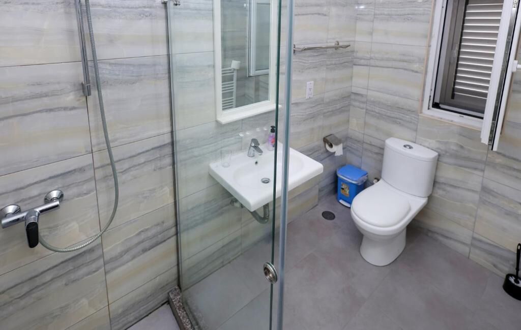 Un bagno con cabina doccia in vetro, lavandino bianco e water.