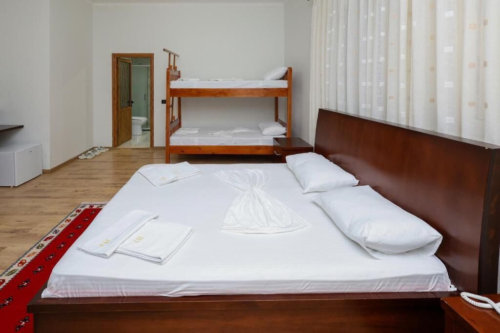 A hotel room with a wooden bed, a bunk bed, a bathroom visible through an open door, and a telephone on the bedside table.