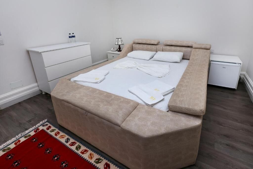 A bedroom with a large bed, a bedside table, a nightstand, a lamp, and a small white cabinet.