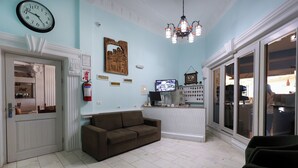 A hotel lobby with a brown sofa, a clock, a television, and a chandelier.