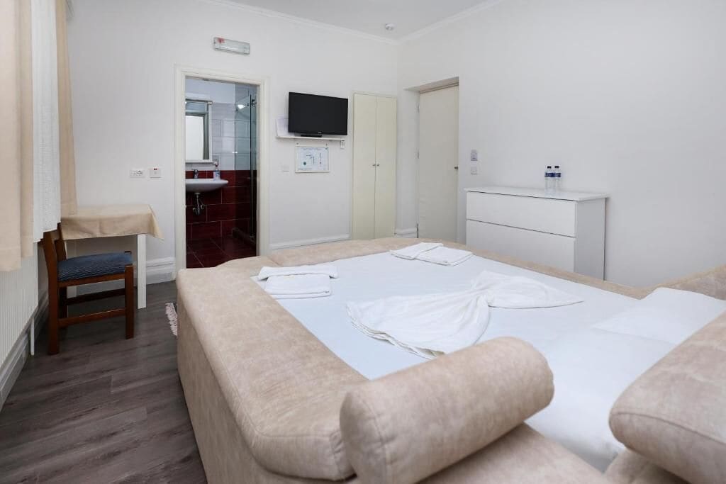 Quarto de hotel com cama, poltrona, televisão, pia e armário.