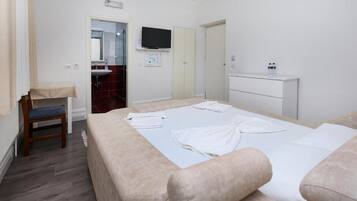 Quarto de hotel com cama, poltrona, televisão, pia e armário.