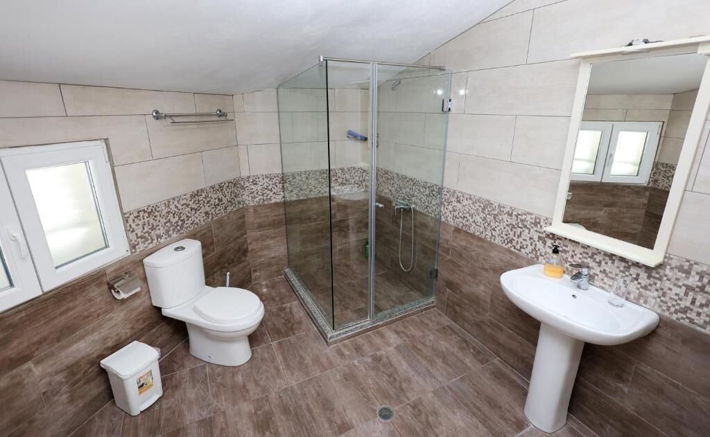 A bathroom with a glass-enclosed shower, a toilet, and a sink.