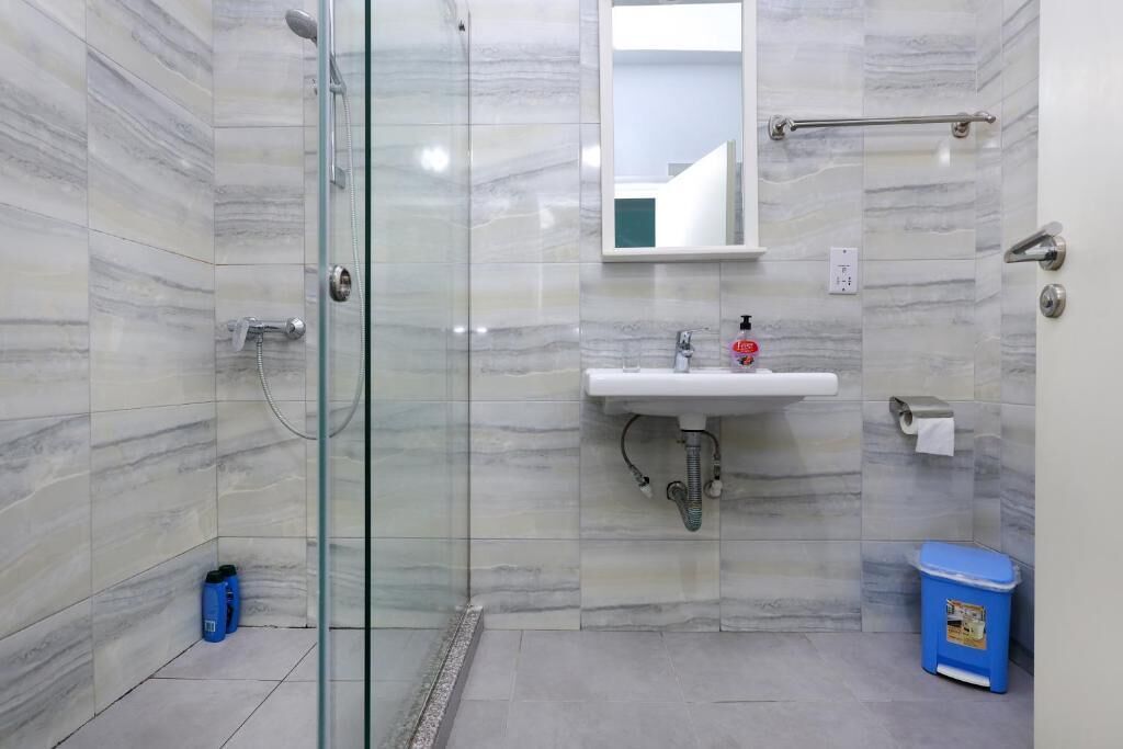 Un baño con cabina de ducha de vidrio, un lavamanos con espejo y un cubo de basura azul.