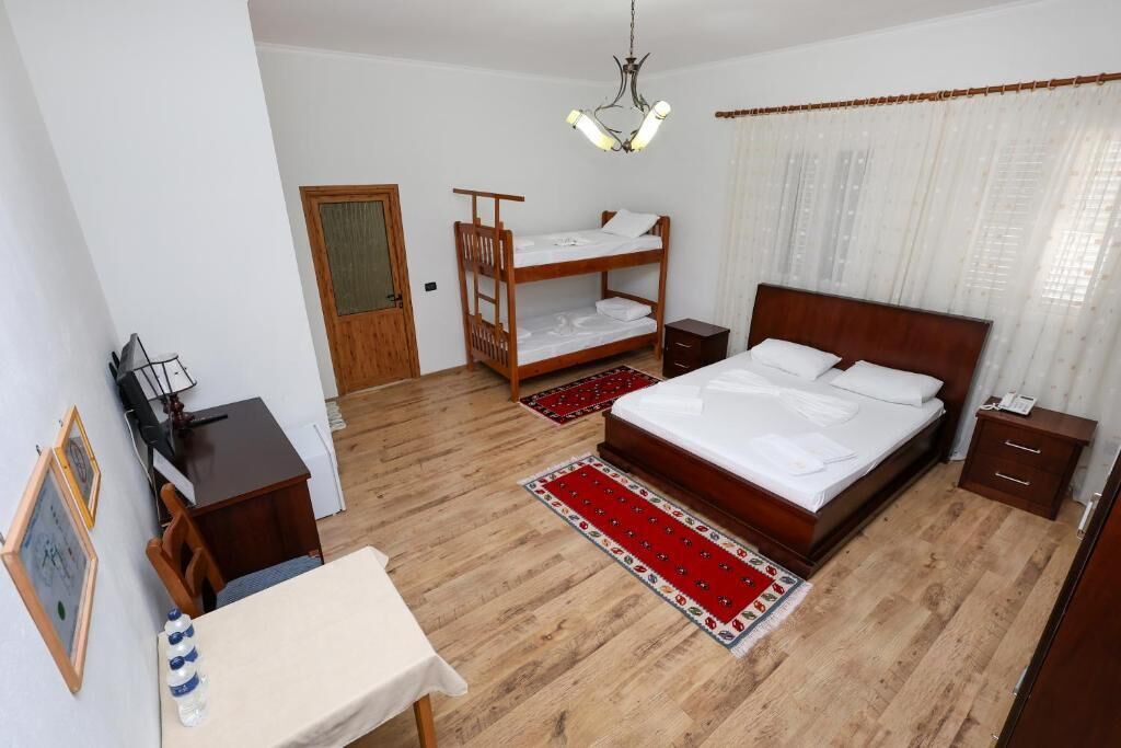 A bedroom with a wooden bunk bed, a single bed, a desk with a chair, and a small table.
