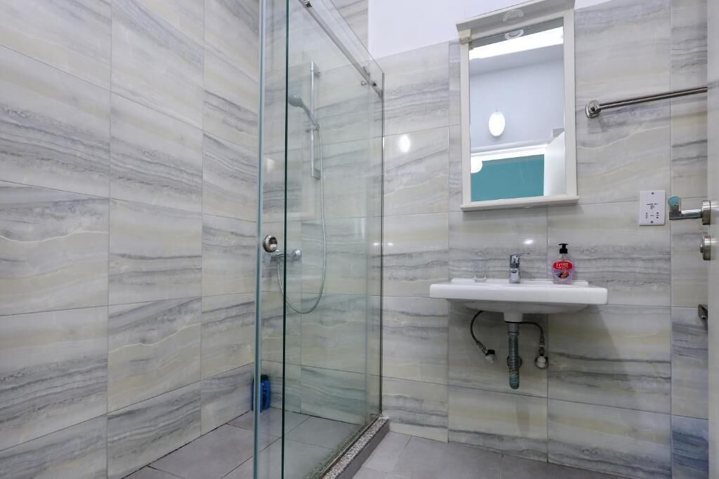 Un baño moderno con cabina de ducha de vidrio, un lavamanos con espejo y dispensador de jabón.