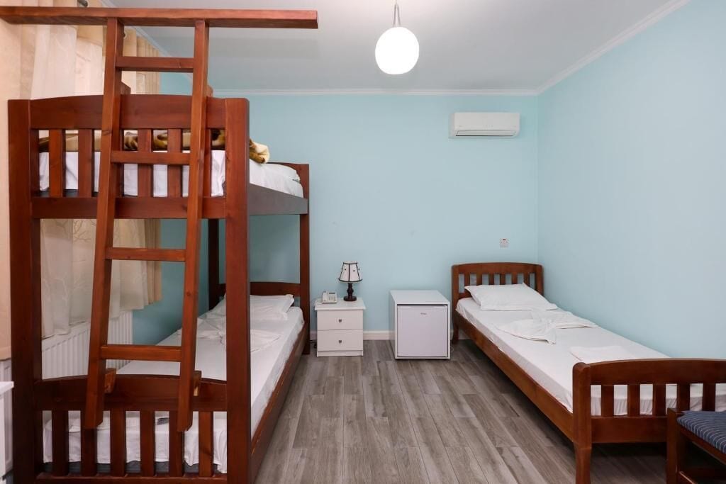 Quarto em dormitório com beliches, mesa de cabeceira, luminária e um pequeno armário branco.