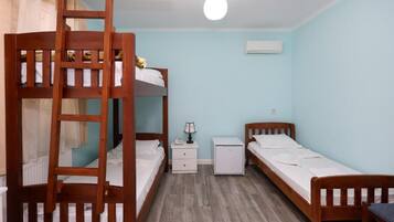 Quarto em dormitório com beliches, mesa de cabeceira, luminária e um pequeno armário branco.