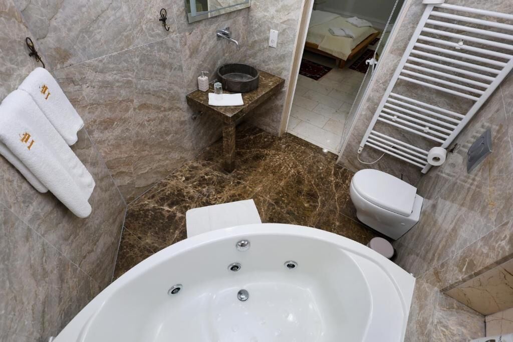Un baño con una bañera grande, un lavamanos y un inodoro. Hay toallas colgadas en la pared y un espejo sobre el lavamanos.