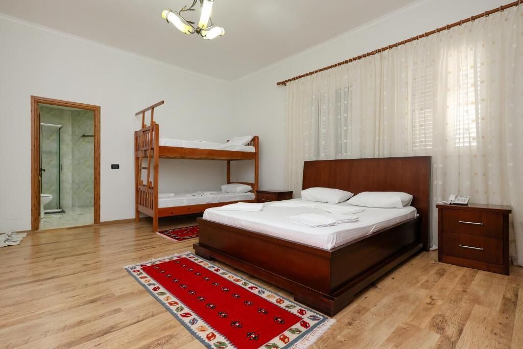 Un dormitorio con una cama litera de madera, una cama individual, una mesita de noche y una alfombra roja estampada.