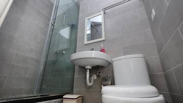 Un baño con cabina de ducha de vidrio, un lavamanos blanco y un inodoro.