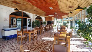 A spacious indoor area with wooden tables and chairs, a counter with a glass display, and large windows allowing natural light.