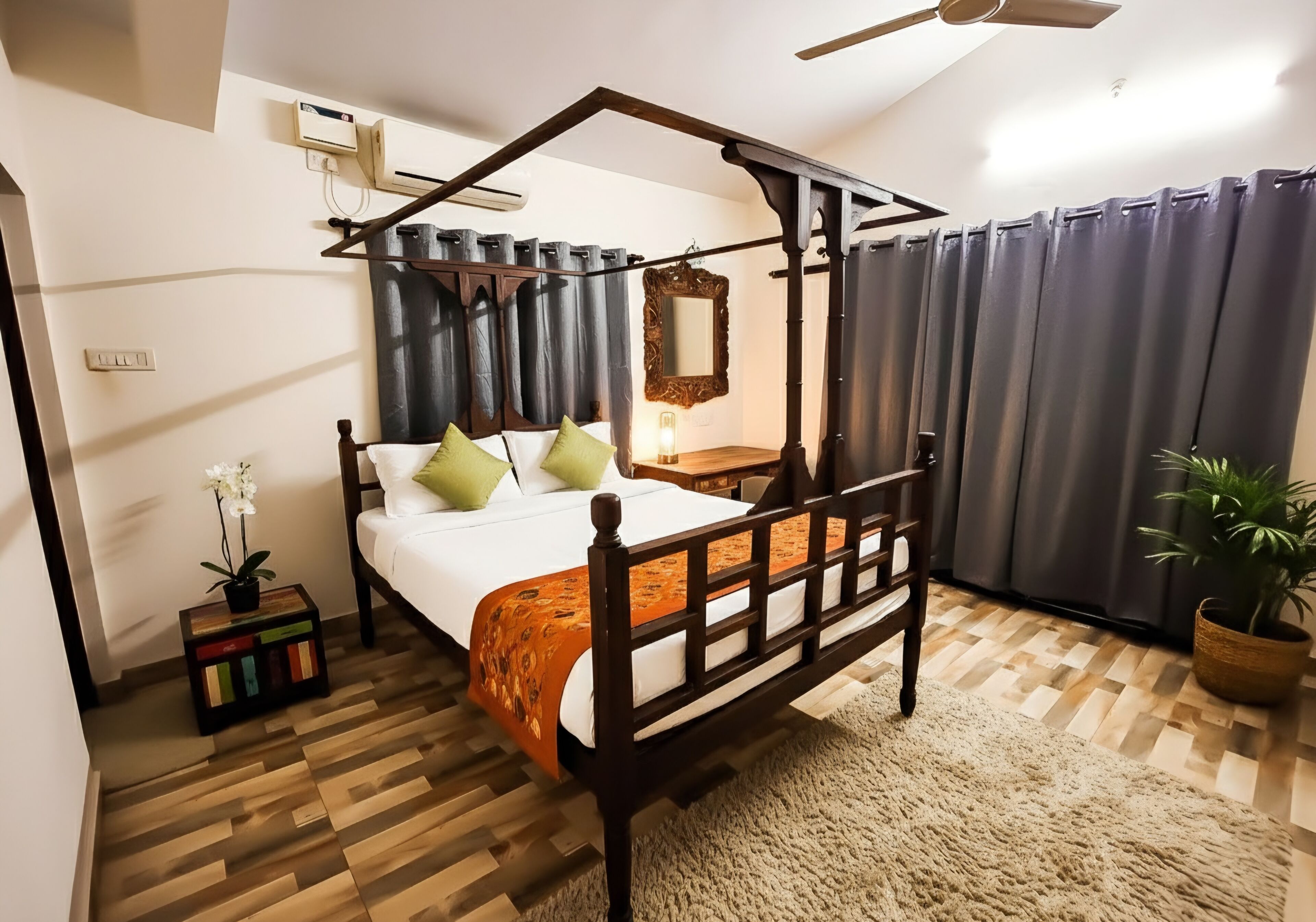 A four-poster bed with a wooden frame, a small bedside table, a nightstand, a potted plant, and a mirror on the wall.
