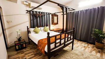 A four-poster bed with a wooden frame, a small bedside table, a nightstand, a potted plant, and a mirror on the wall.