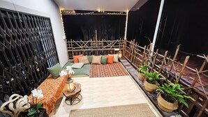 A cozy balcony with a sofa, cushions, a patterned table, and potted plants. - The Plix Villa (Vagator)