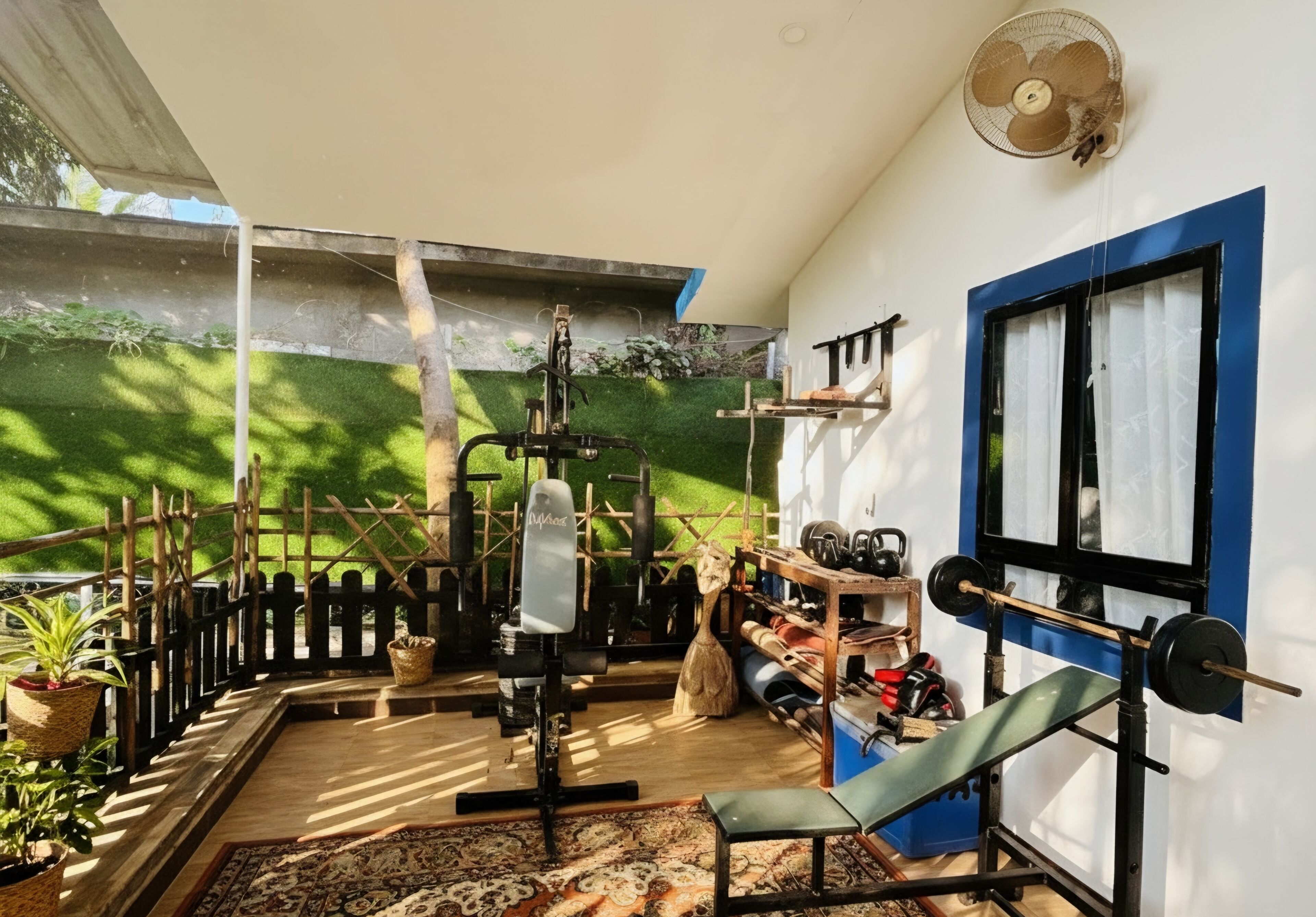 Un gimnasio en casa con equipo de ejercicio, un ventilador y una ventana con cortinas.