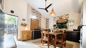 A modern kitchen with a dining area, featuring a wooden table and chairs, a ceiling fan, and a patterned backsplash. - The Plix Villa (Vagator)