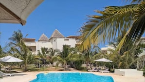 A swimming pool with clear blue water, surrounded by palm trees and lounge chairs. - Tranquil Villa Apartment in Papa Remo Village-2326 (Watamu)