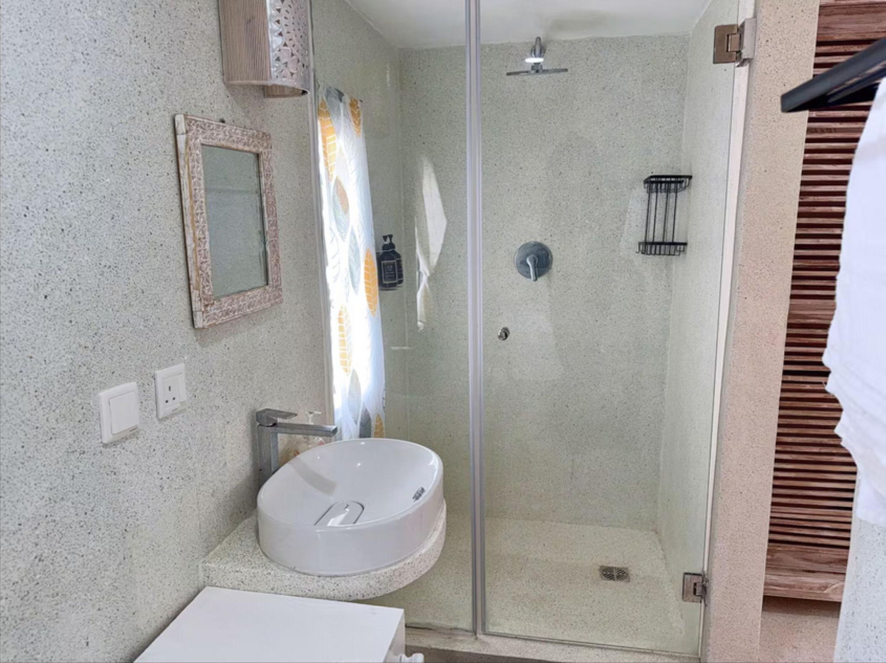 A bathroom with a glass-enclosed shower, a white sink, and a mirror with a decorative frame.