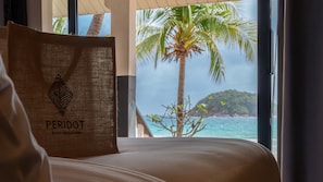 Een bed met uitzicht op de oceaan en een palmboom. Op het bed ligt een bruine tas met de tekst 