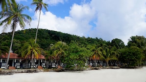 Ein Strandresort mit Palmen, einem Sandstrand und einer bewaldeten Hügelkette im Hintergrund.