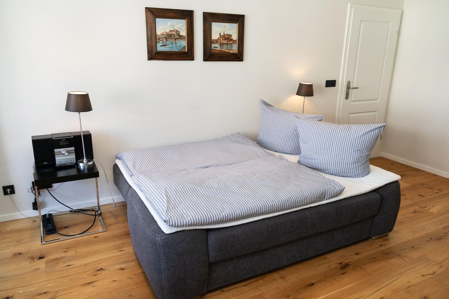 A bedroom with a bed, two bedside lamps, a small table with a lamp, and two framed pictures on the wall.