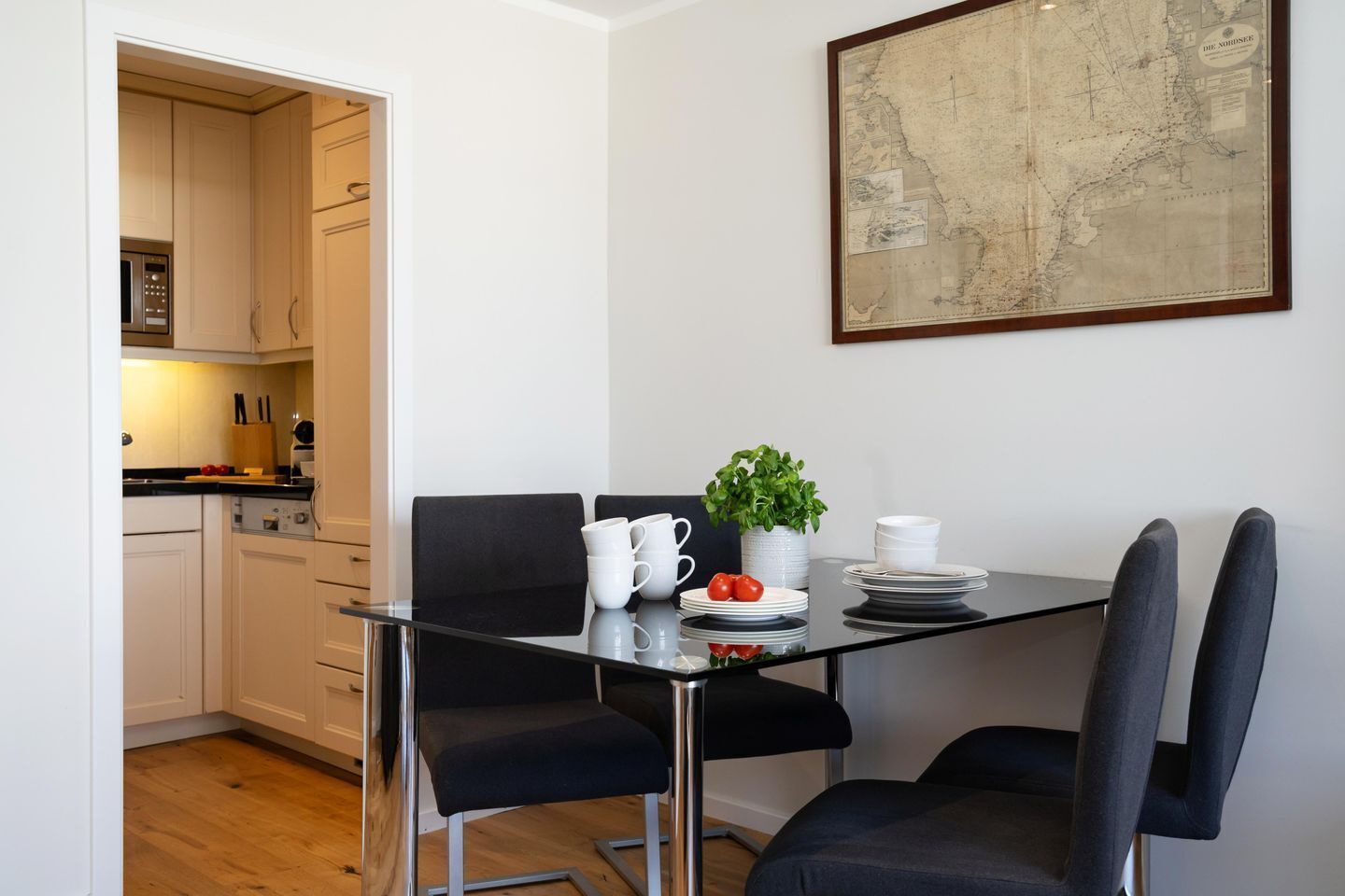 Un coin repas avec une table en verre, des chaises noires, des assiettes blanches et une plante en pot.