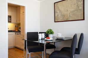 A dining area with a glass table, black chairs, white plates, and a potted plant. - North Sea - Modern and central 2-room apartment with balcony, WLAN. Pets (Sylt)