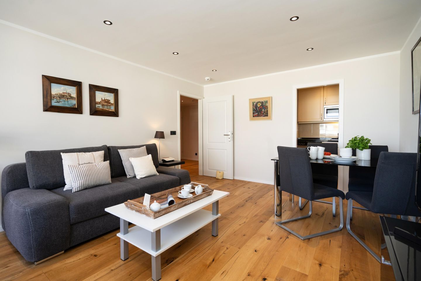 A modern living room with a grey sofa, a coffee table, and a dining area with chairs and a table.