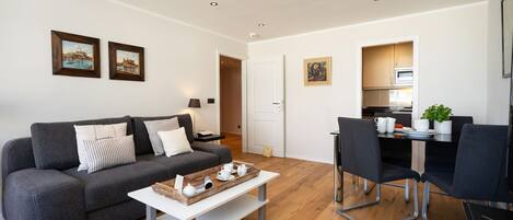 A modern living room with a grey sofa, a coffee table, and a dining area with chairs and a table.