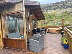 A wooden cabin with a deck, outdoor seating, and a hot tub. - Peaceful 1-bedroom cottage in Hvalfjarðarsveit by the Lake (Hvalfjarðarsveit)