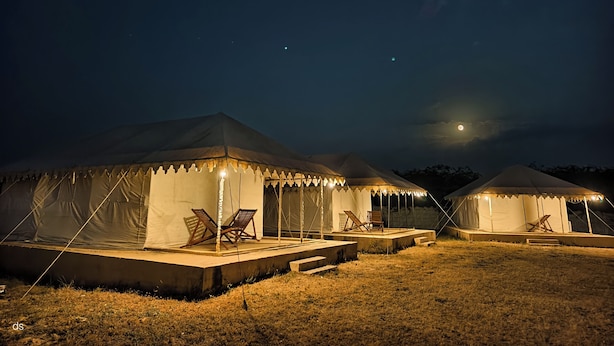 Deux tentes, dotées de plateformes et de chaises intégrées, installées sur une pelouse, de nuit.