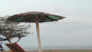 Une plage avec un parasol en bois et une chaise rouge.