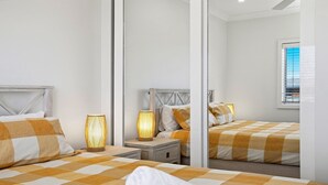 Ein Schlafzimmer mit zwei Betten, jeweils mit einer karierten Bettdecke, einem Nachttisch mit Lampe und einem großen Spiegel, der den Raum reflektiert.