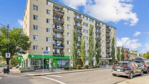 En flervåningsbyggnad med lägenheter, en grön fasad, en övergångsskylt för fotgängare och en parkerad bil på gatan.