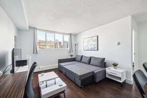 Ein modernes Wohnzimmer mit Sofa, Esstisch, Fernseher und Blick auf die Stadt.