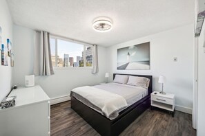 Ein modernes Hotelzimmer mit Bett, Nachttisch, Lampe und Blick auf die Stadt durch das Fenster.
