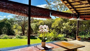 A wooden table with a potted orchid, a ceiling fan, and a view of a lush garden. - Luxury 5 bed Home in Juliasdale - 2309 (Juliasdale)