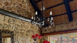 A dining area with a stone wall, a chandelier, and red flowers on a table. - Luxury 5 bed Home in Juliasdale - 2309 (Juliasdale)