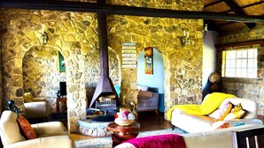 A stone-walled living room with a fireplace, white leather sofas, and a rustic ceiling. - Luxury 5 bed Home in Juliasdale - 2309 (Juliasdale)