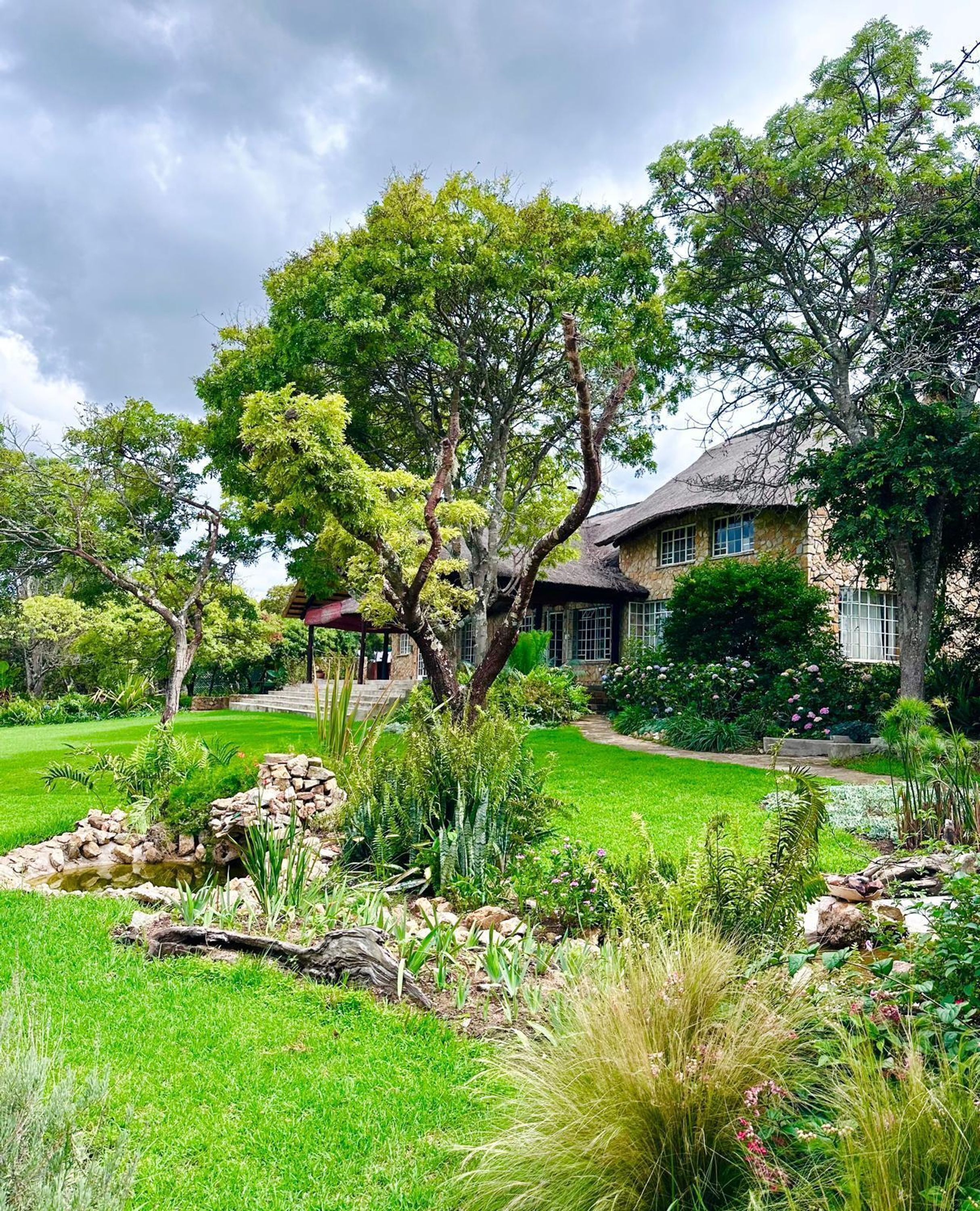 Una casa con un jardín cuidado, un estanque y un gran árbol en el patio delantero.