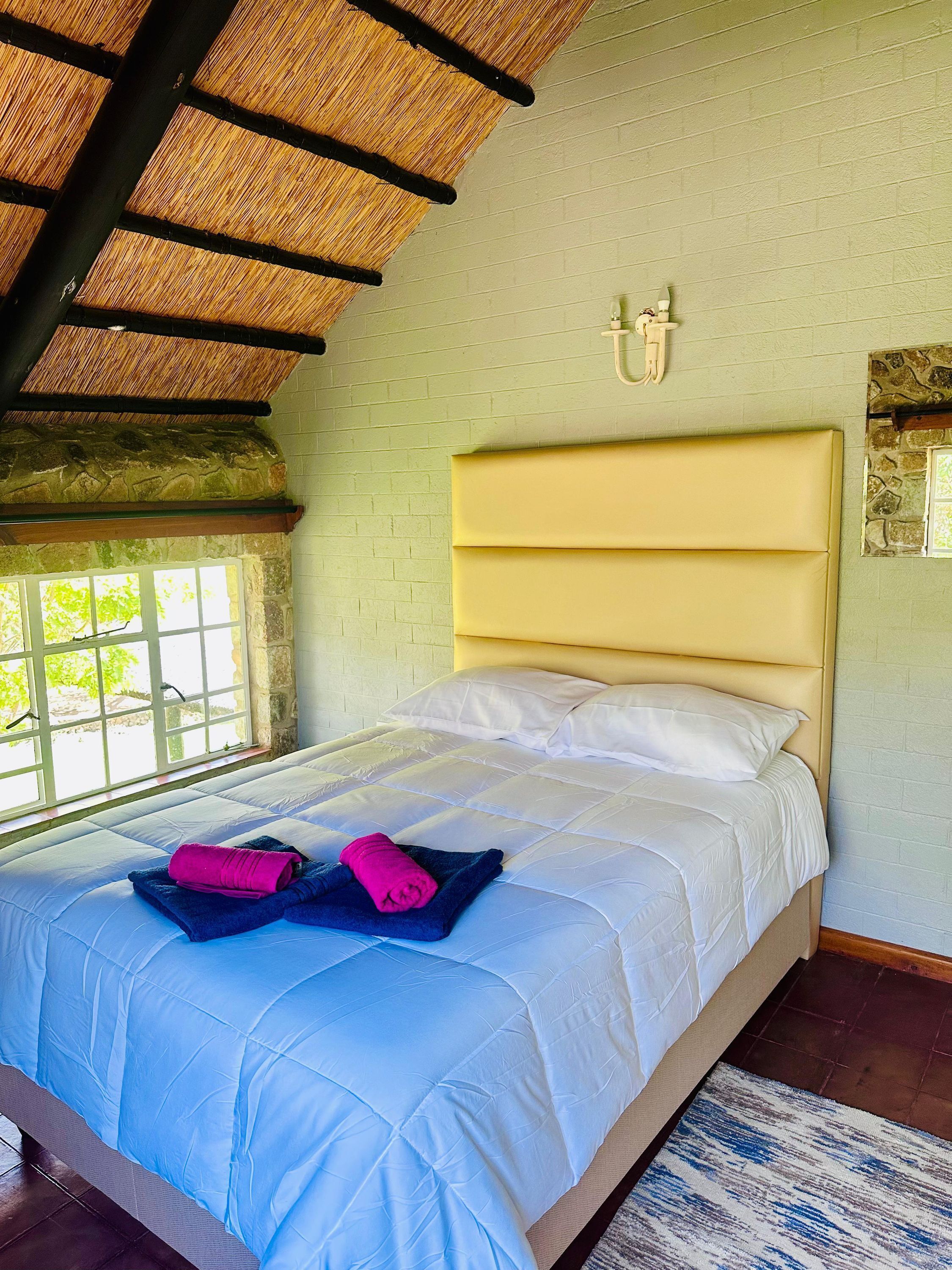 A bed with a headboard, a window with a view, and a stone wall.