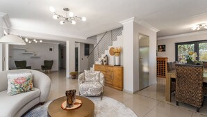 Ein großzügiger Wohnbereich mit Sofa, Sessel und Couchtisch. Eine Treppe führt zu einem Essbereich mit Holztisch und Stühlen.